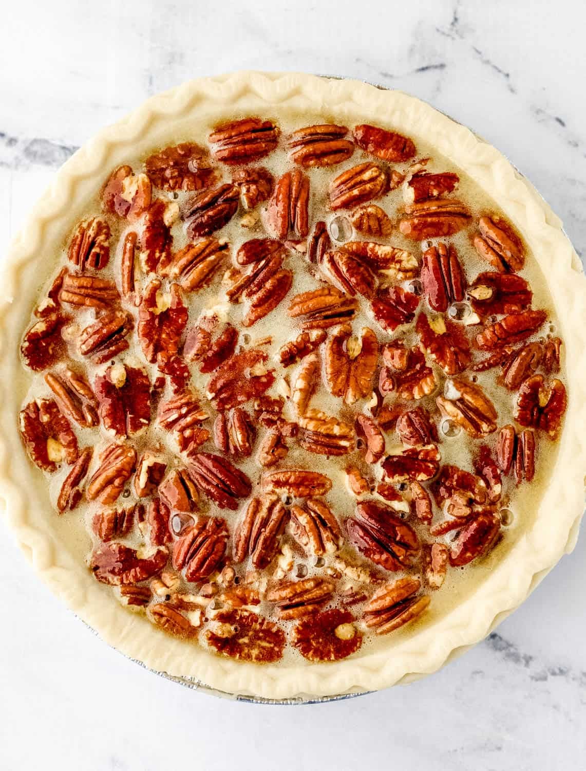 Overhead view of pecan mixture added to pie crust dough.