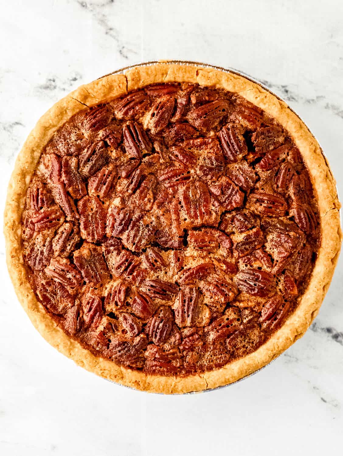 Overhead view of finished pecan pie recipe on marble surface.