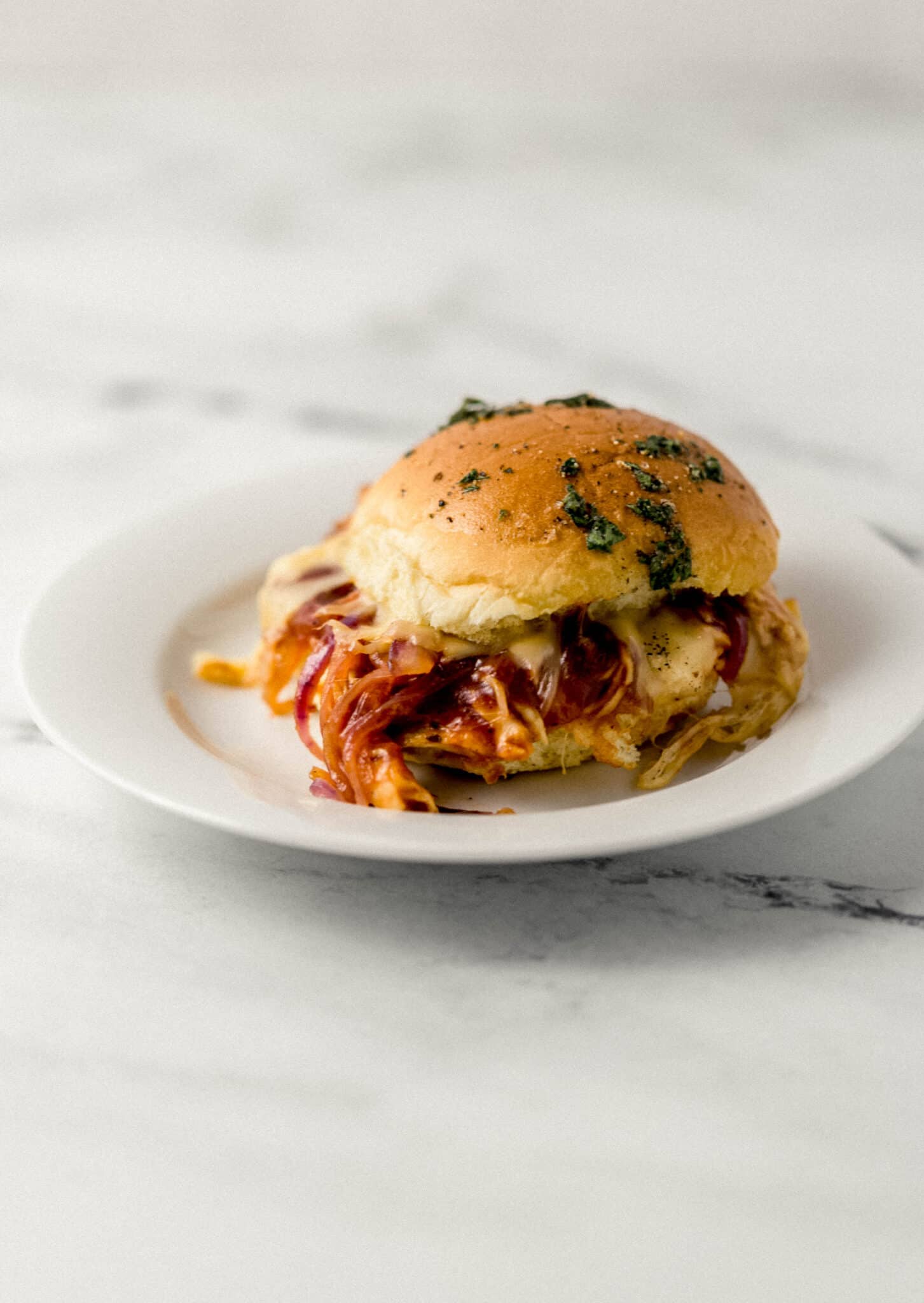 close up side view of single chicken slider on white plate 