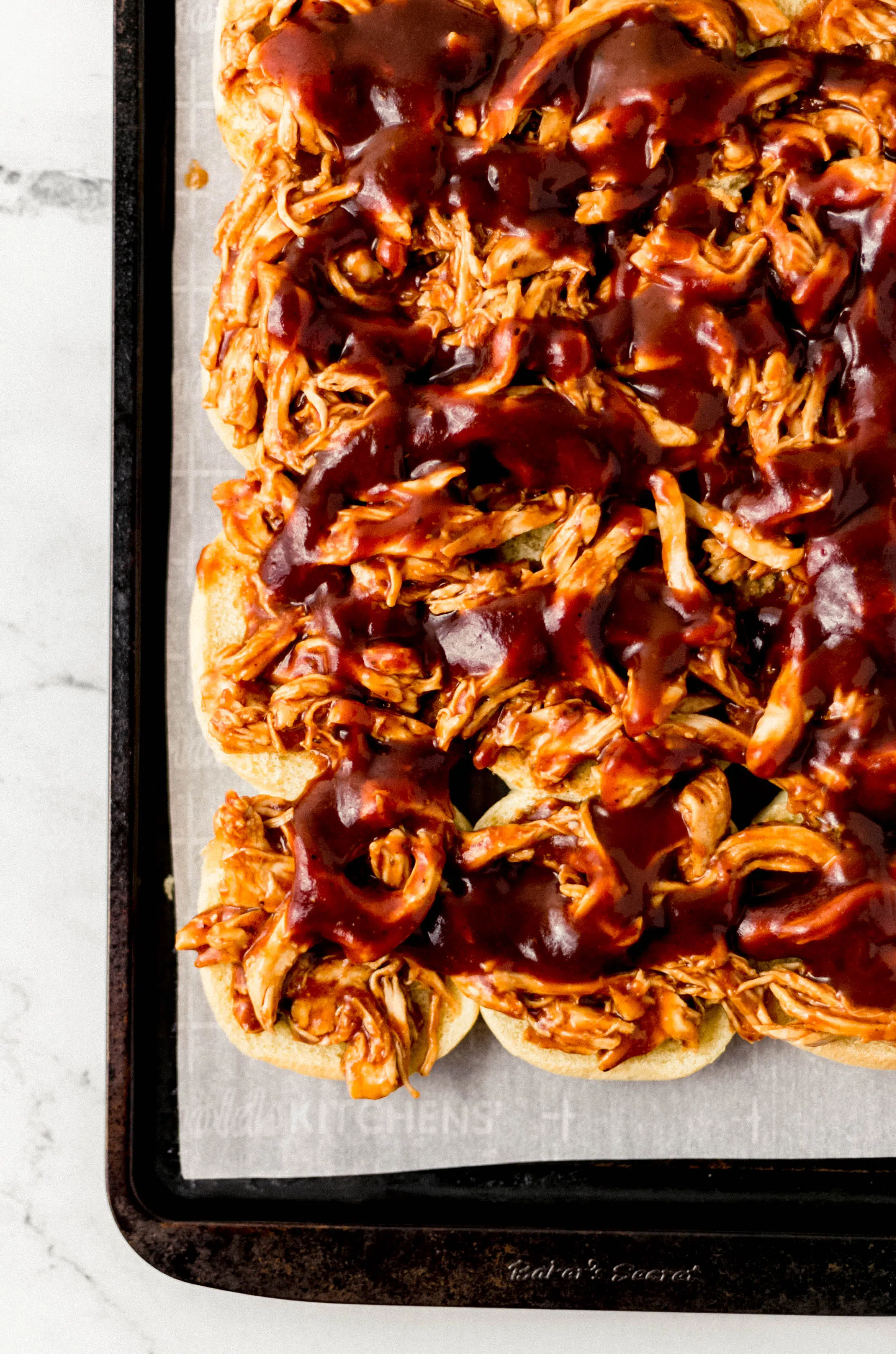 shredded chicken and bbq sauce spread over the bottom of slider buns on parchment lined sheet pan