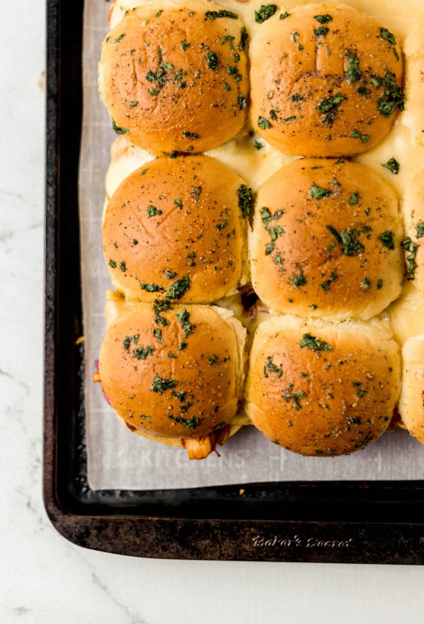 finished chicken sliders on parchment lined sheet pan topped with butter sauce 