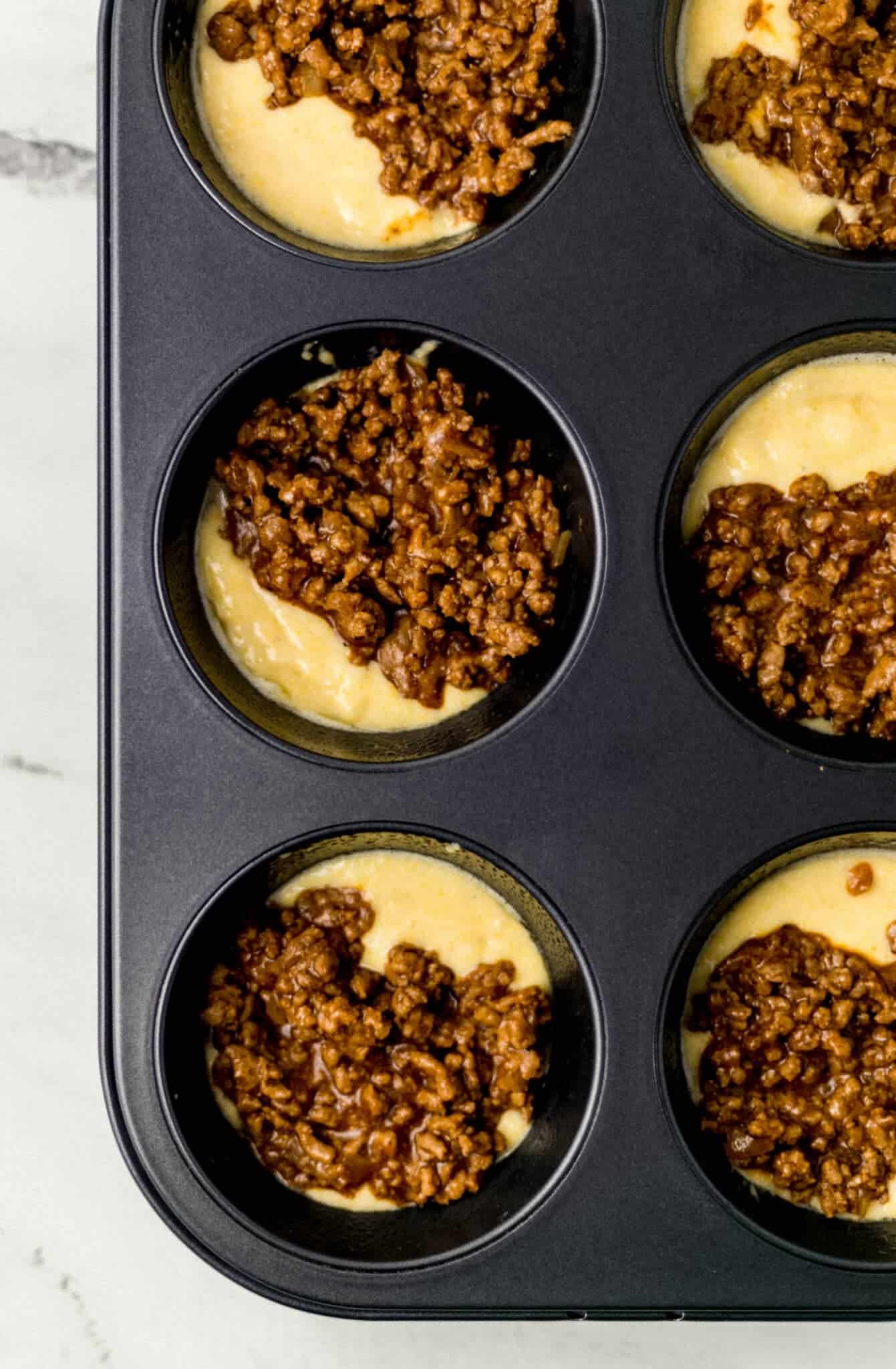 cornbread and meat mixture combined in muffin pan before baking