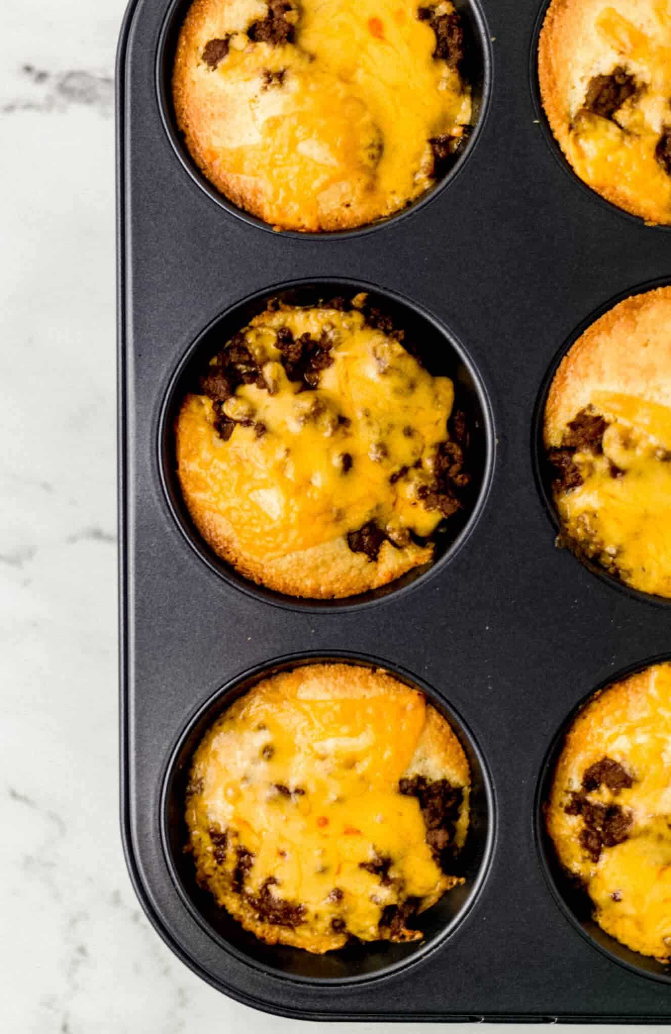 overhead view of barbecue cornbread muffins in muffin pan topped with melted cheese 