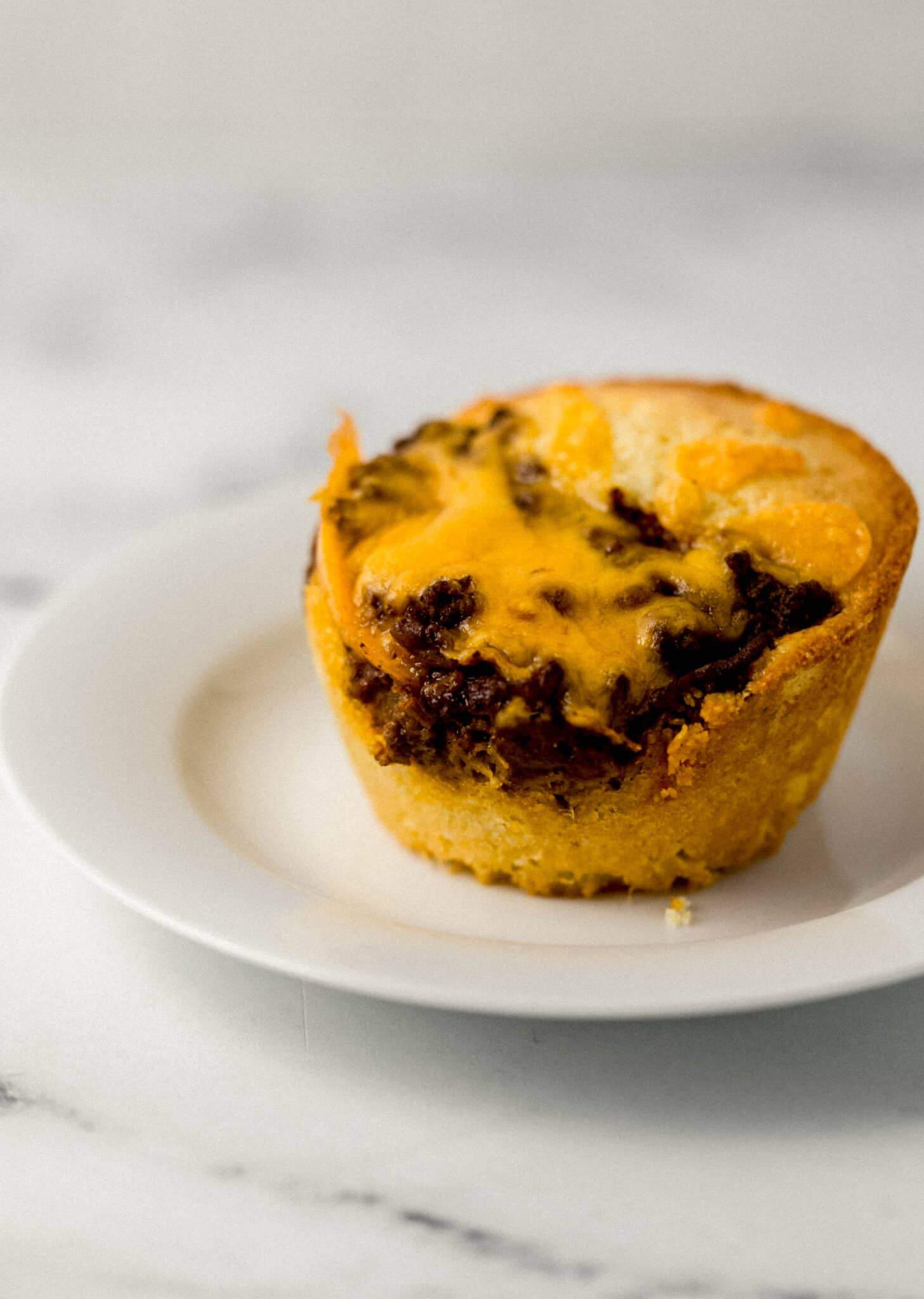 close up side view of single cornbread muffin on white plate