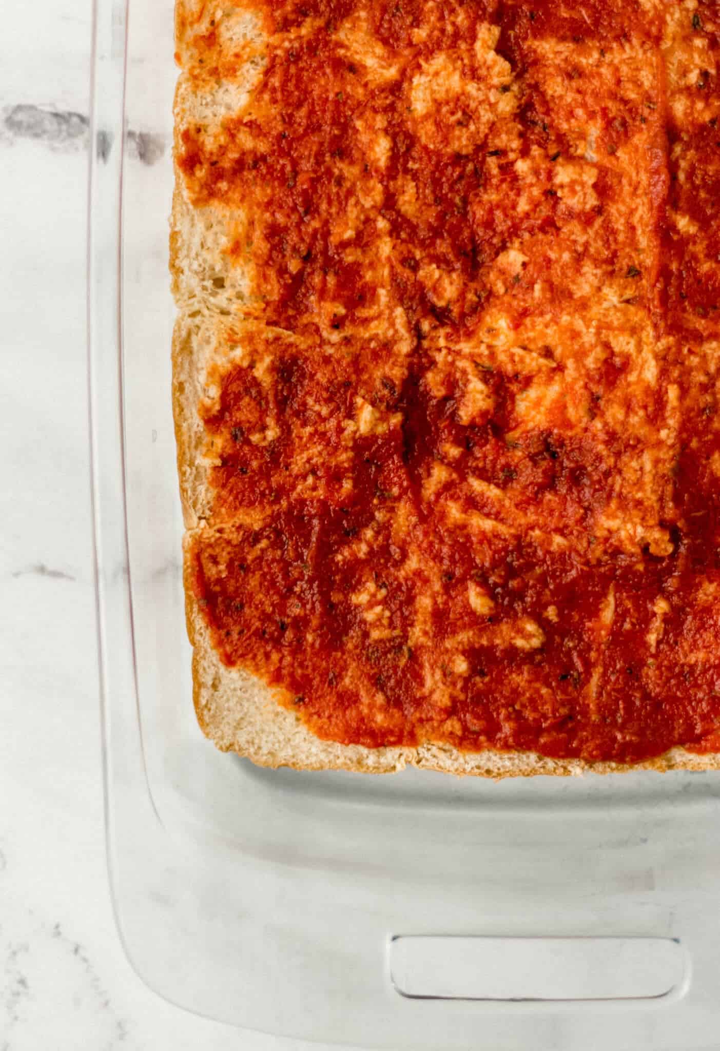 pizza sauce spread on bottom half of dinner rolls in glass baking dish