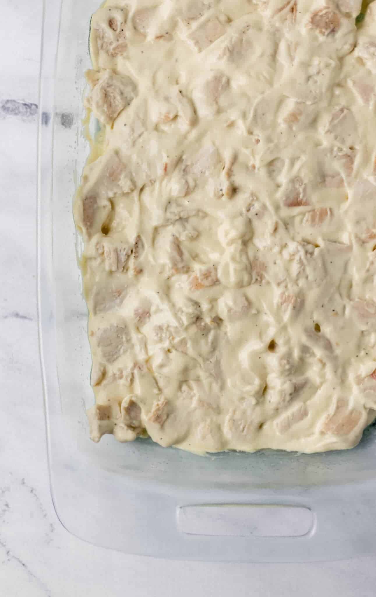 creamy chicken mixture added to the bottom of a glass baking dish 