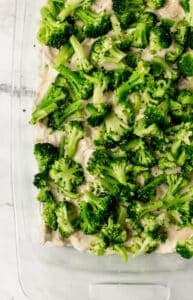 Broccoli added to other casserole ingredients in glass baking dish.