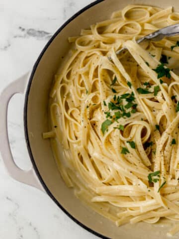 overhead view of finished fettuccine alfredo recipe in large skillet topped with parsley and ground black pepper