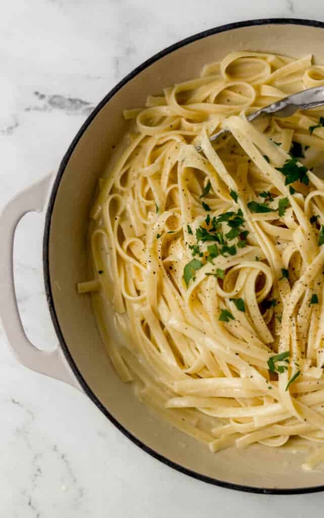 overhead view of finished fettuccine alfredo recipe in large skillet topped with parsley and ground black pepper