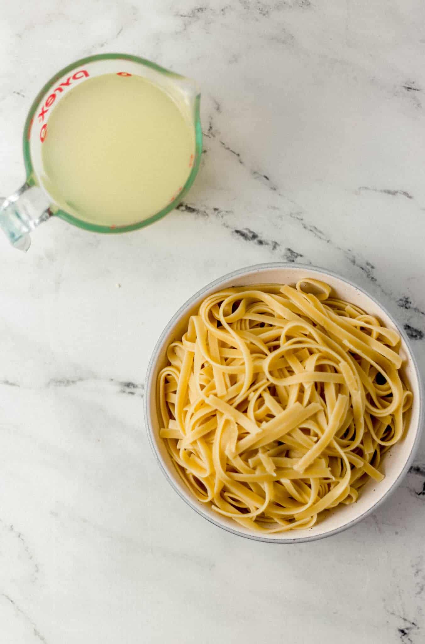 cooked pasta in a bowl and pasta water in a glass measuring cup