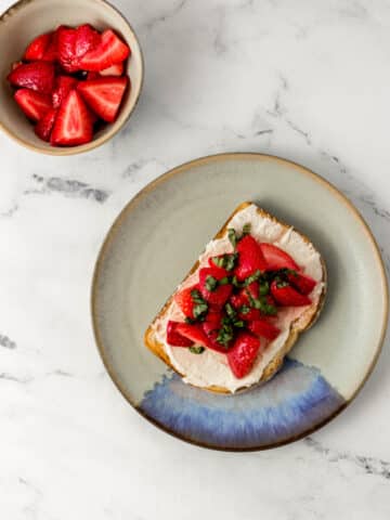 overhead view of strawberry cream cheese toast on plate beside a bowl of strawberries