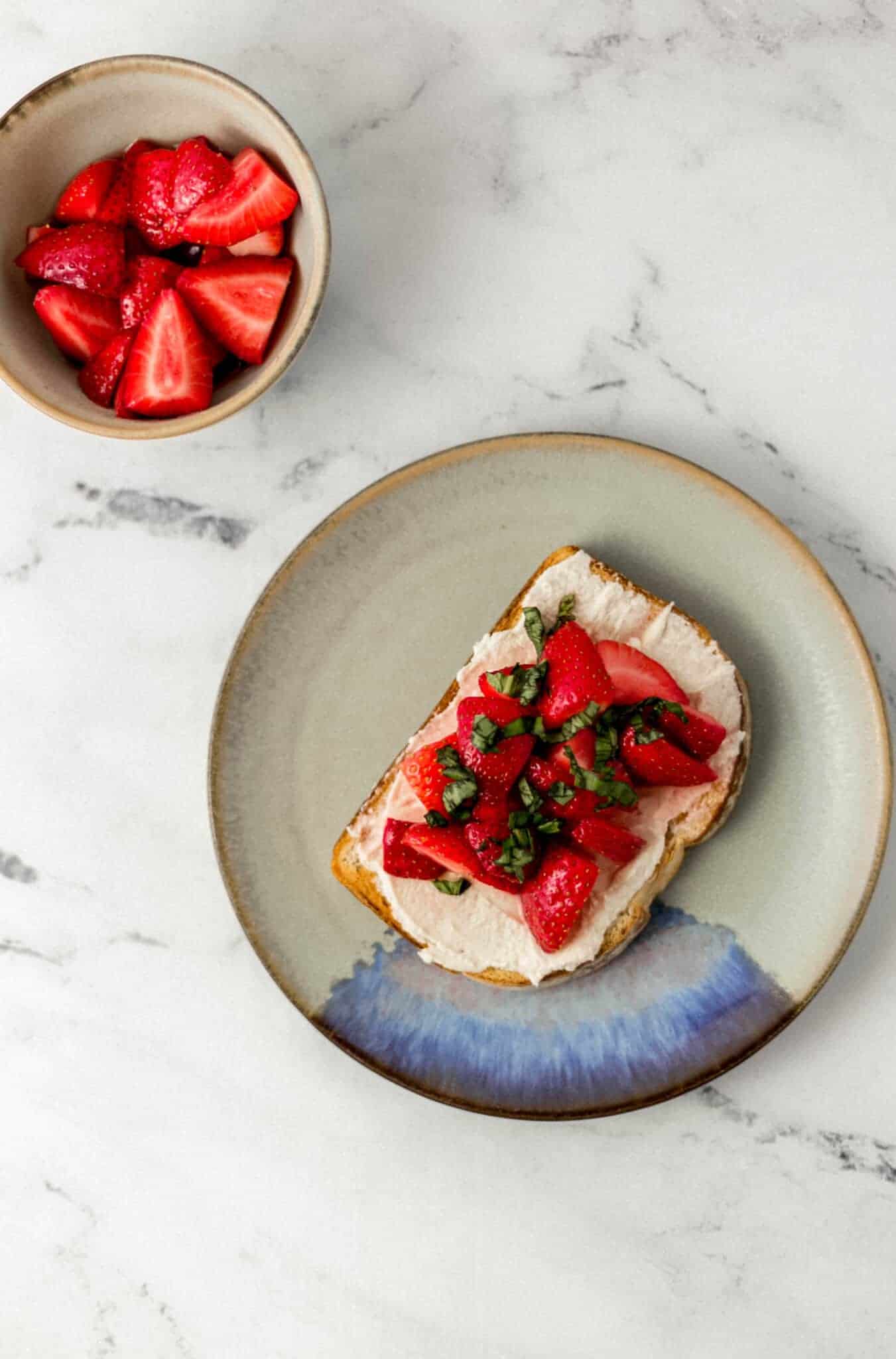 overhead view of strawberry cream cheese toast on plate with a bowl of strawberries beside it