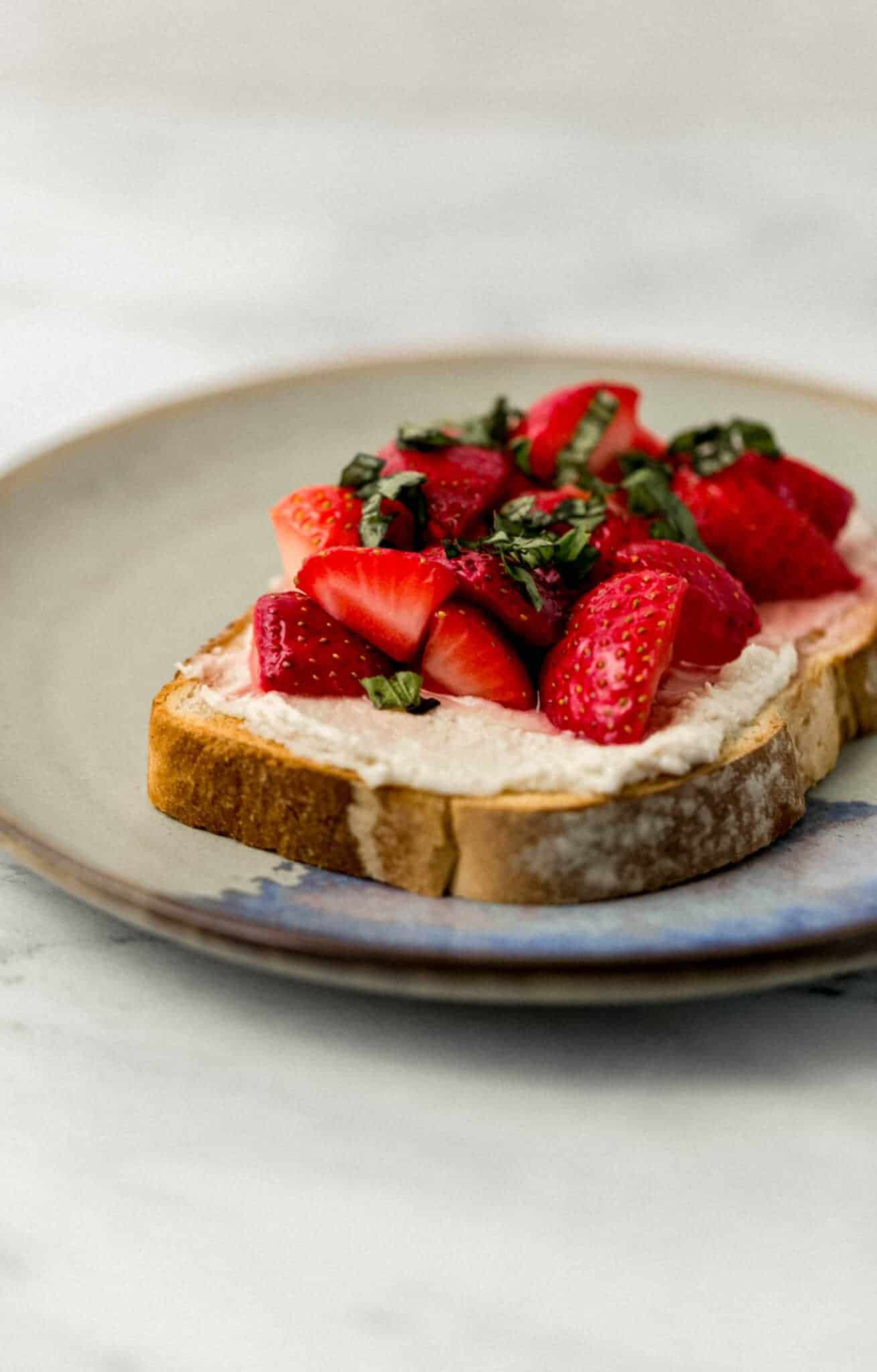 close up side view of finished toast topped with strawberries and basil on a plate 