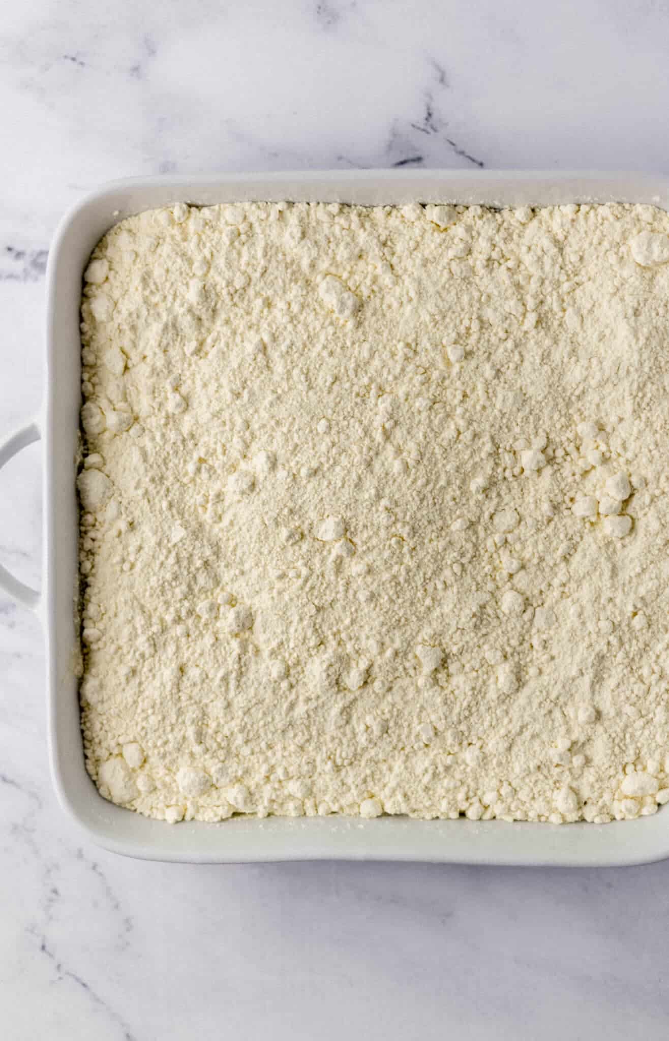 cake mix spread on top of apple pie filling in white baking dish