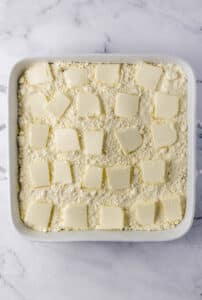 Slices of butter added to other cake ingredients in baking dish.