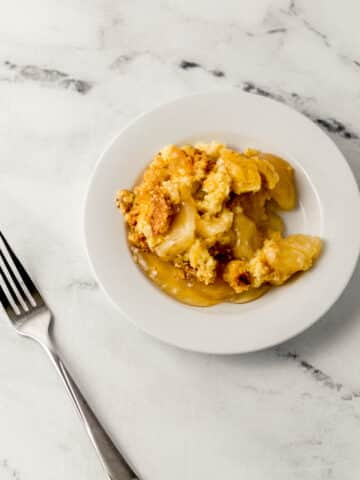 overhead view of single serving of apple dump cake on small white plate beside a fork