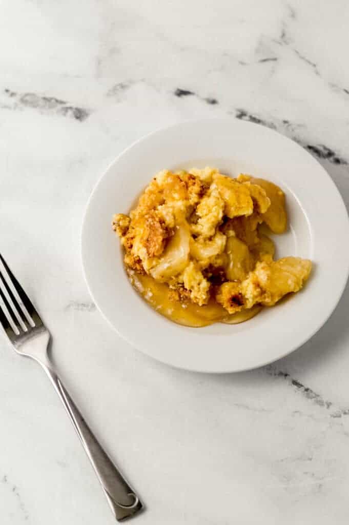 overhead view of single serving of apple dump cake on small white plate beside a fork