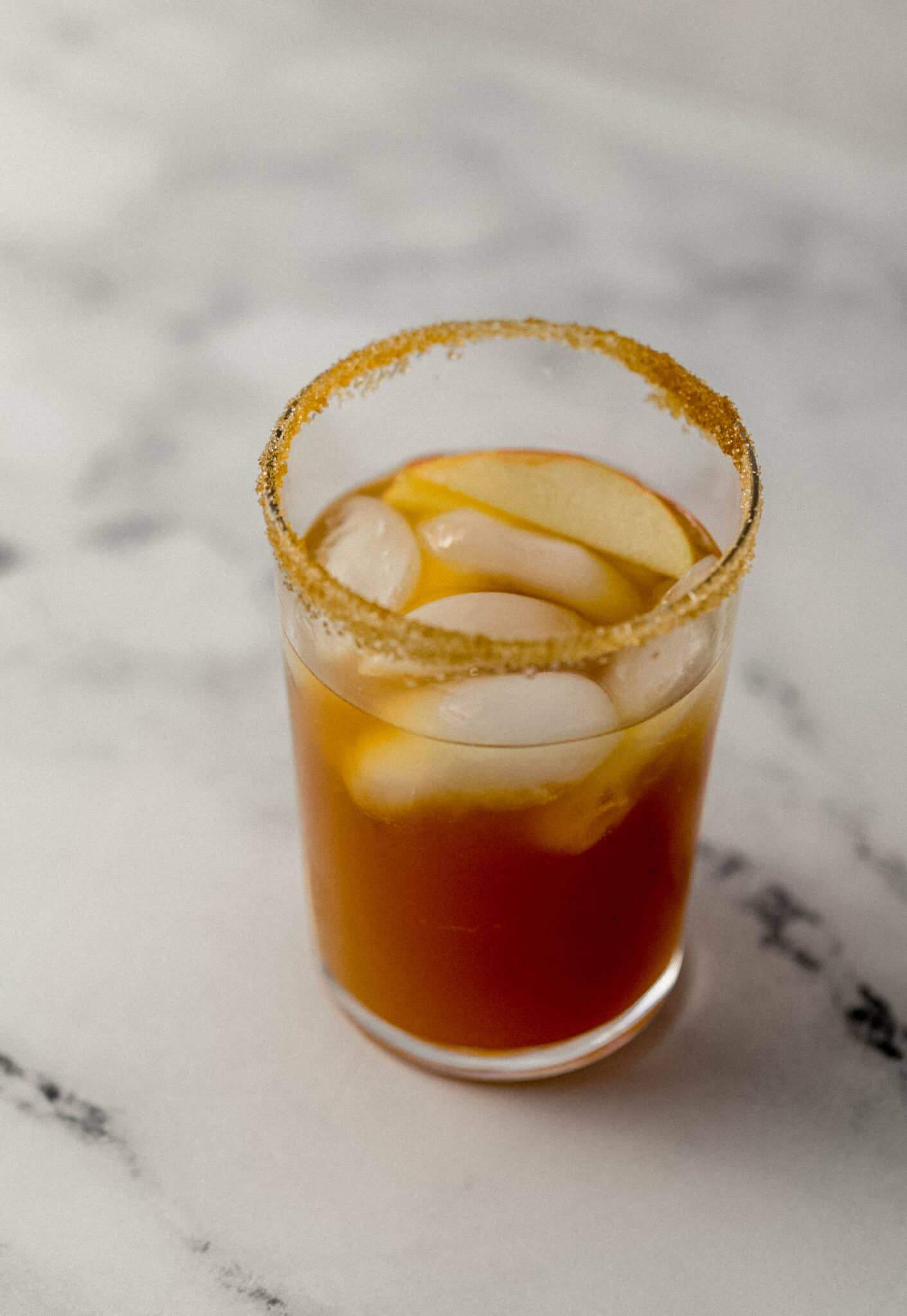 close up side view of margarita in a glass with ice and a slice of apple