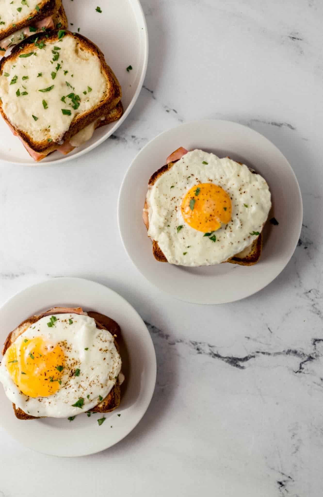 overhead view of finished croque madame sandwiches on white plates on marble surface 