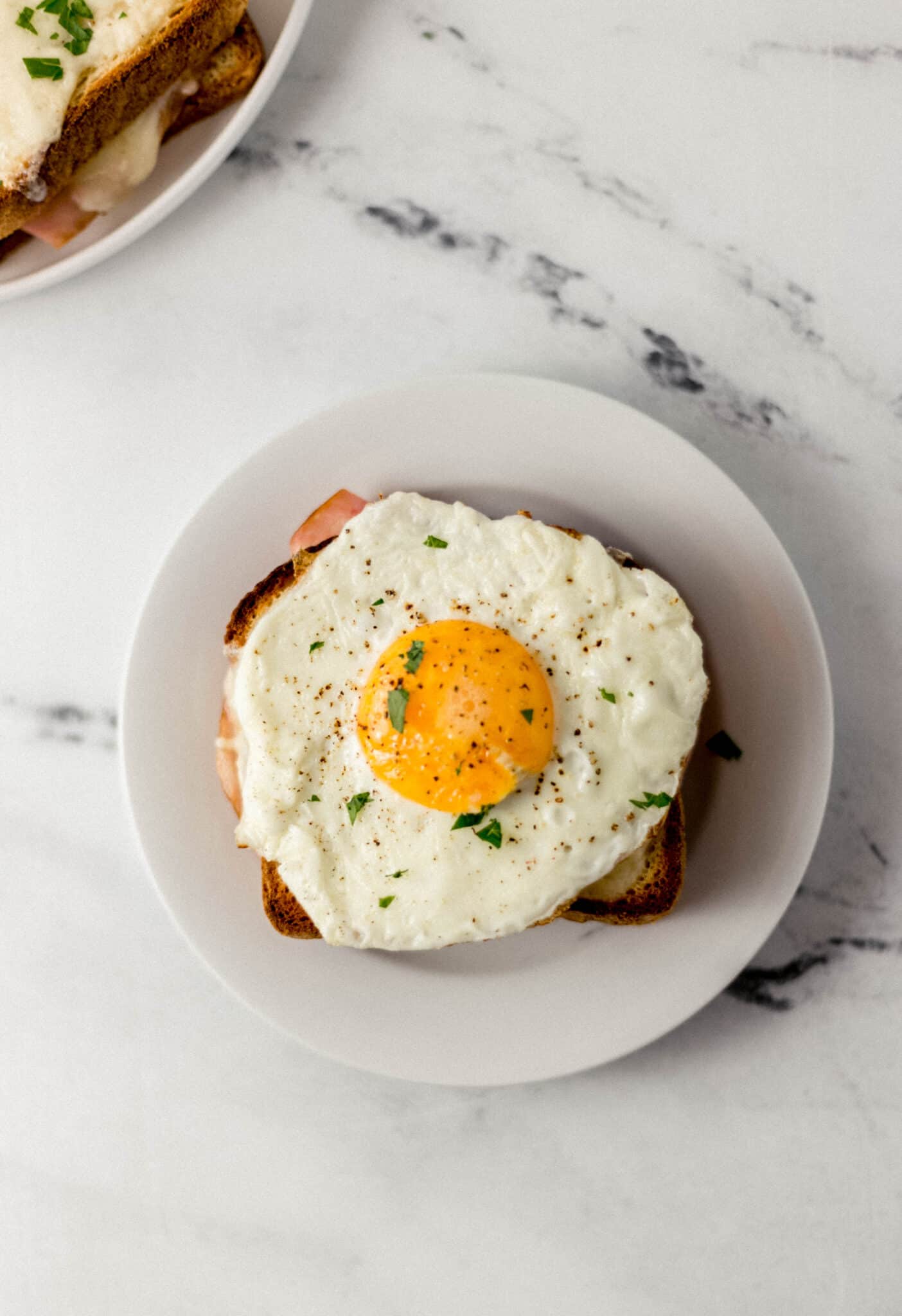 overhead view of finished sandwich topped with egg on small white plate 