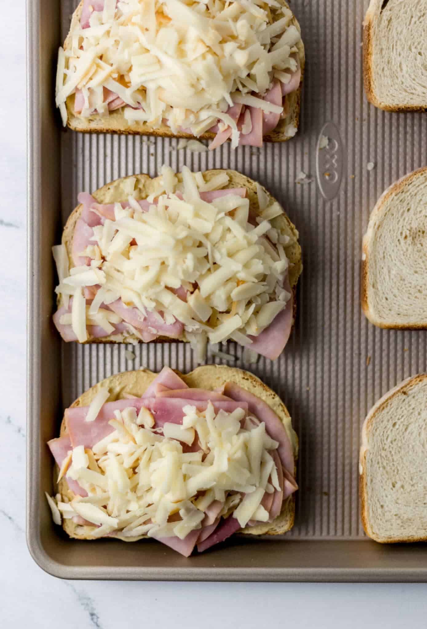 toasted bread topped with mustard, ham, and cheese on sheet pan 