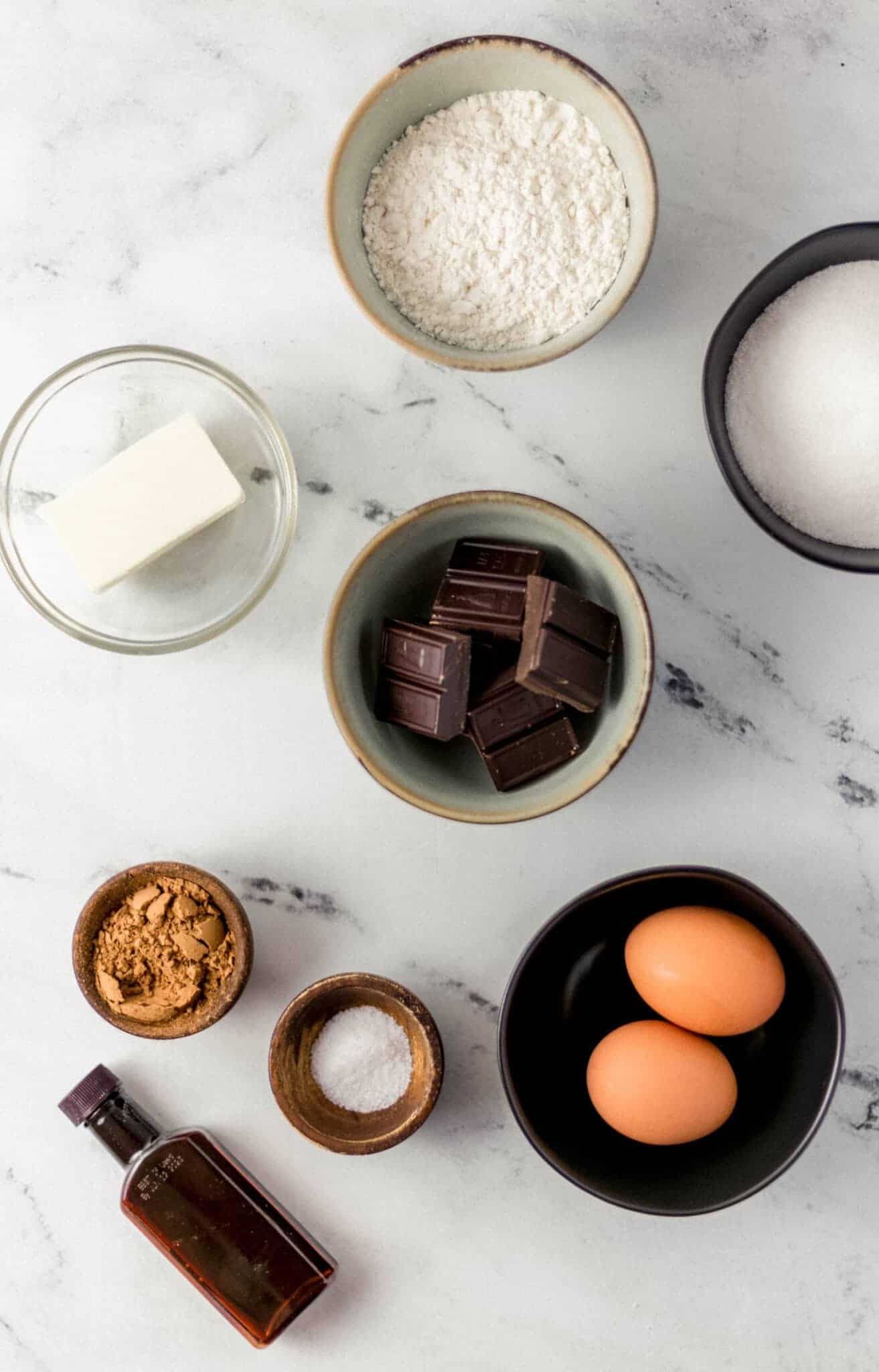 overhead view of ingredients needed to make brownies in separate bowls on marble surface