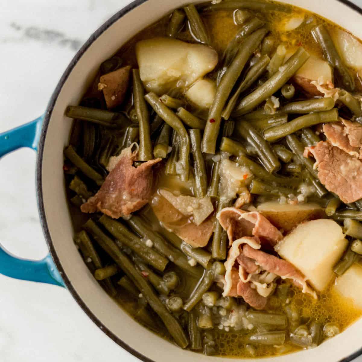 Close up view of finished green beans in large pot on marble surface.