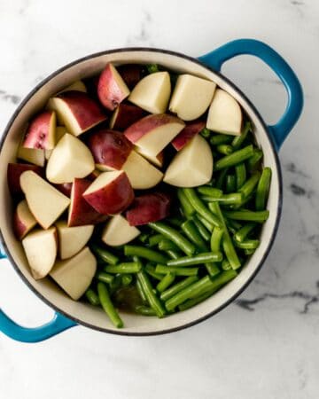 Overhead view of green beans and potatoes added to Dutch oven.