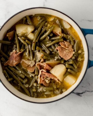 Close up view of finished green beans in large pot on marble surface.