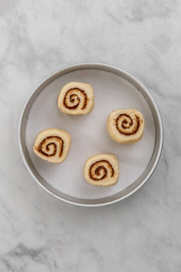 Four cinnamon rolls in parchment lined baking pan.