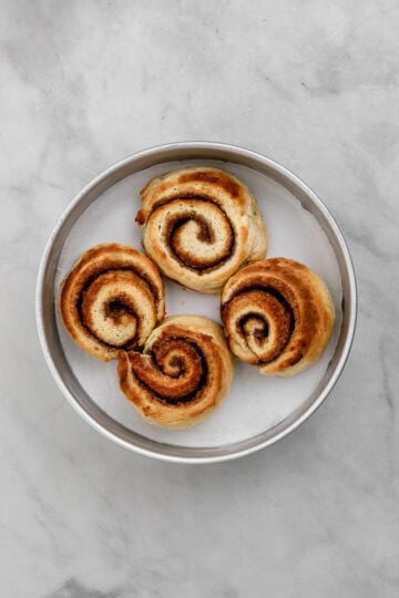 Four baked cinnamon rolls in parchment lined baking pan.