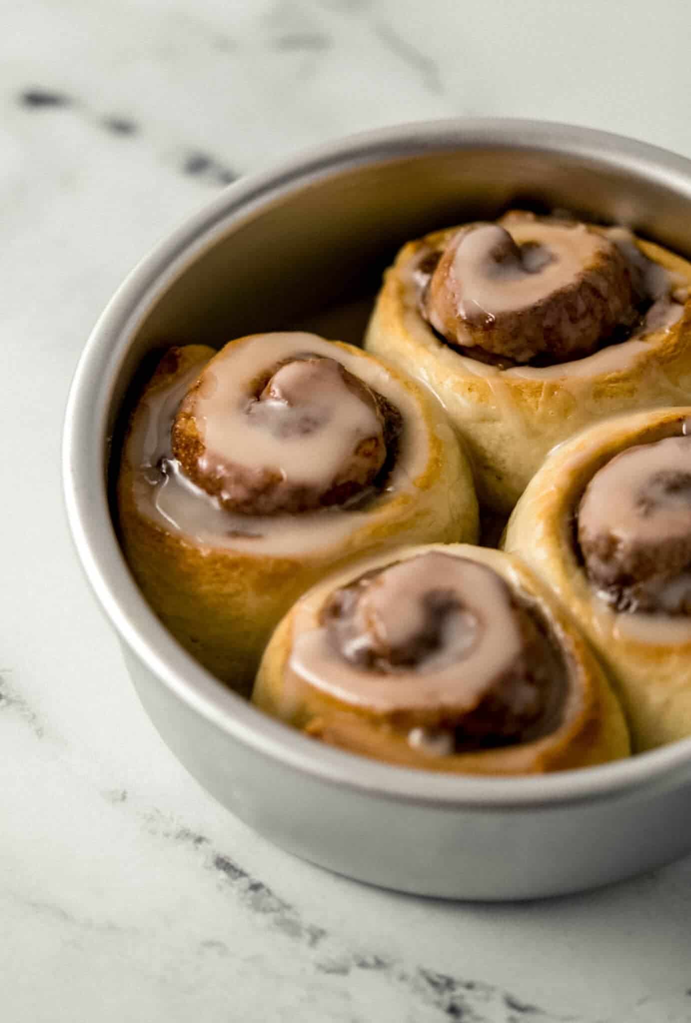 close up side view of four cinnamon rolls in baking pan topped with icing