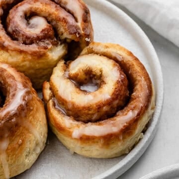 Close up view of cinnamon rolls on white plate by a cloth napkin.