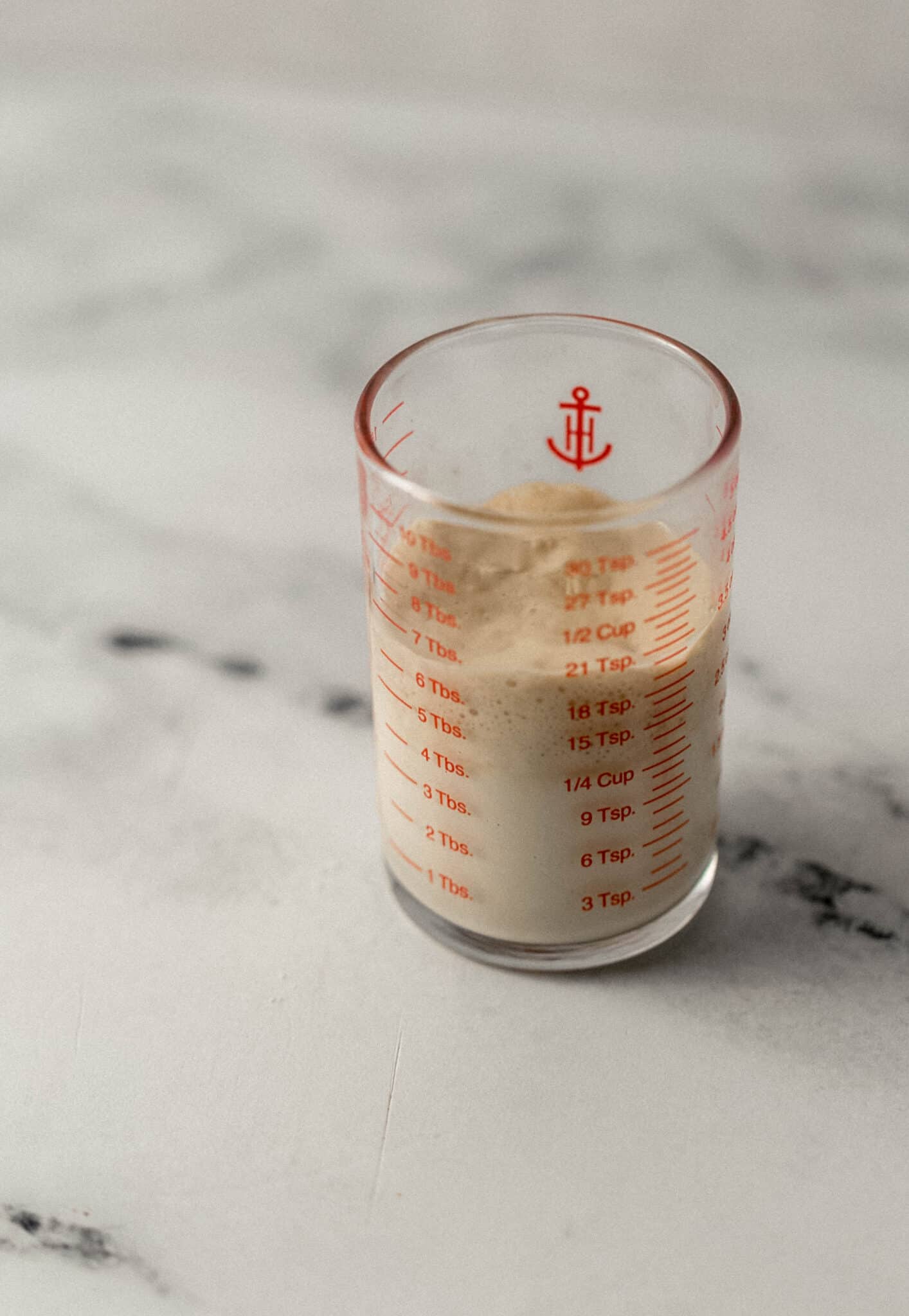 close up side view of warm milk, yeast, and sugar combined in glass measuring cup