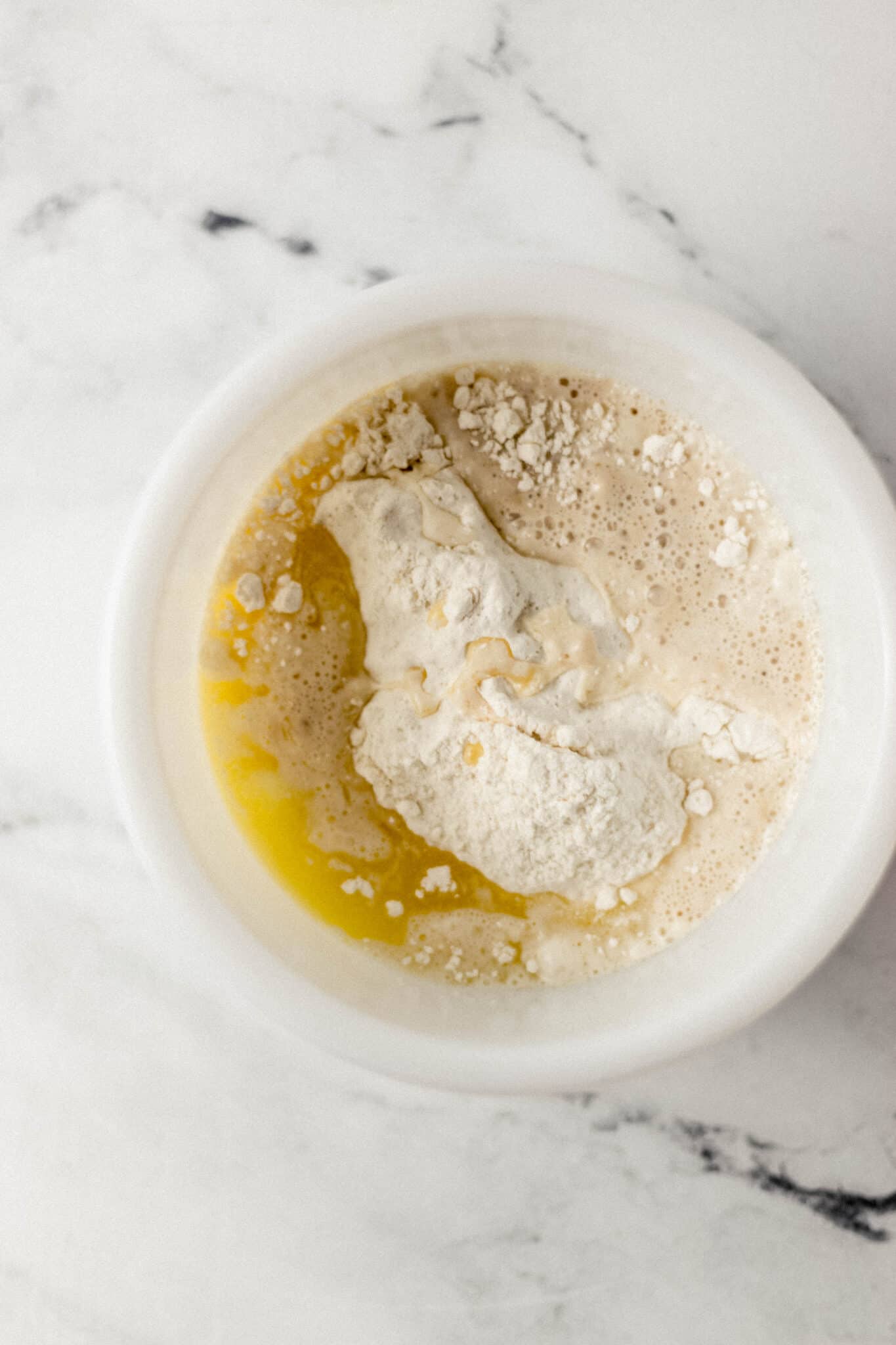 yeast mixture, combined with flour mixture and melted butter in white mixing bowl 