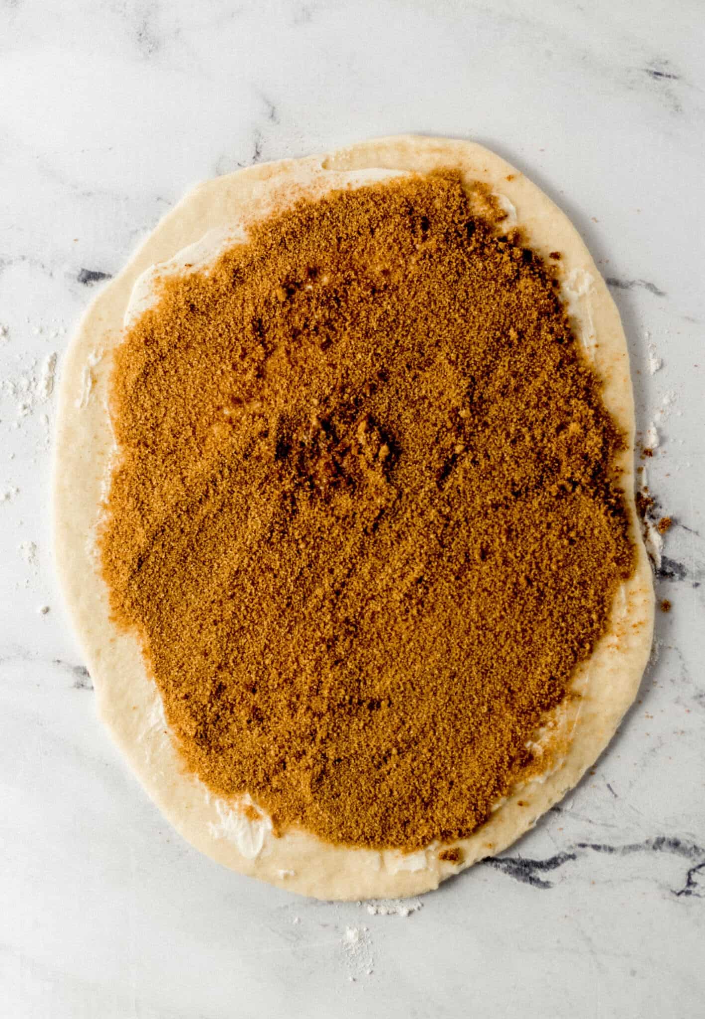 dough rolled out on marble surface and topped with butter, cinnamon and brown sugar