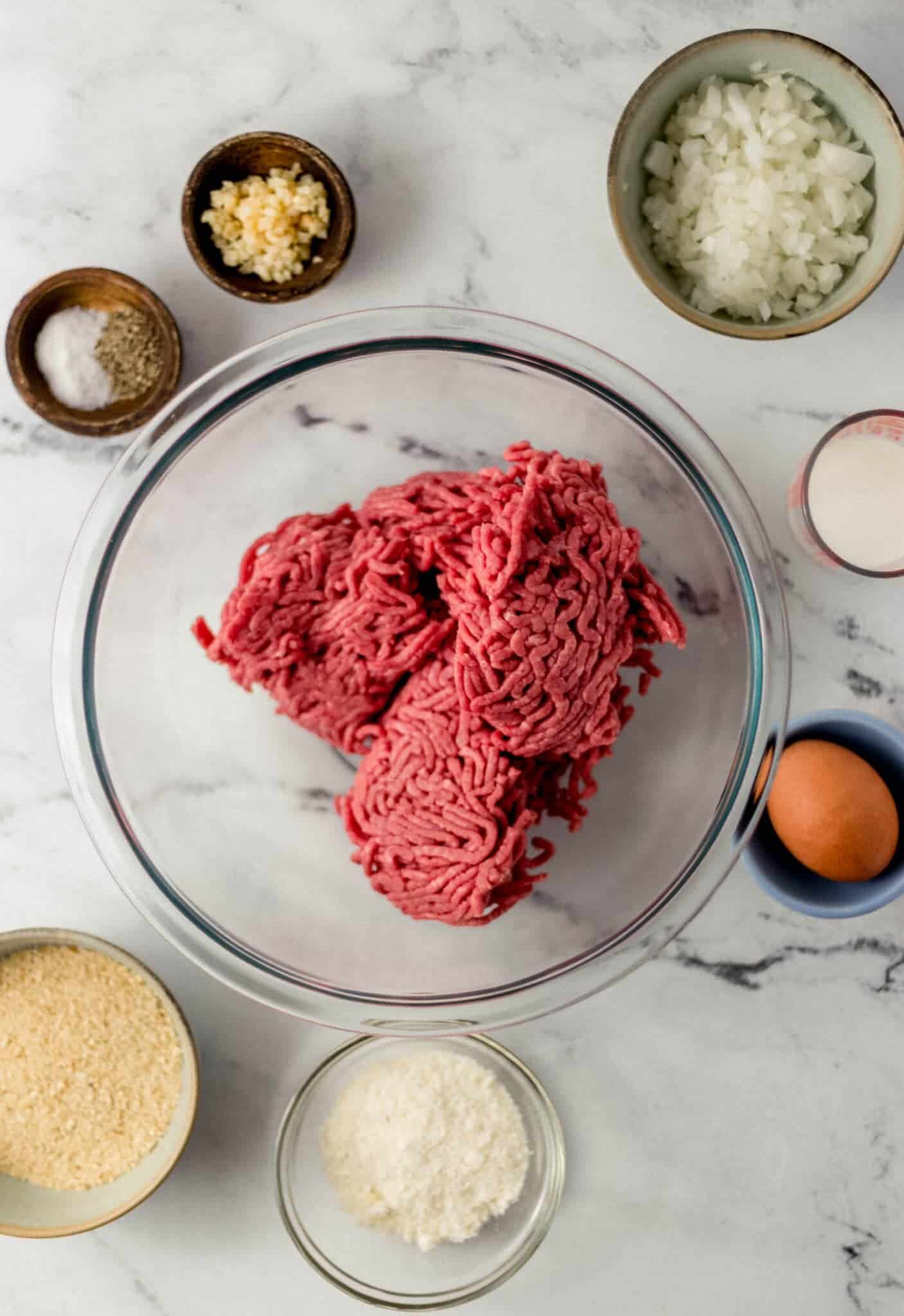 ingredients needed for spaghetti and meatballs in separate bowls on marble surface 