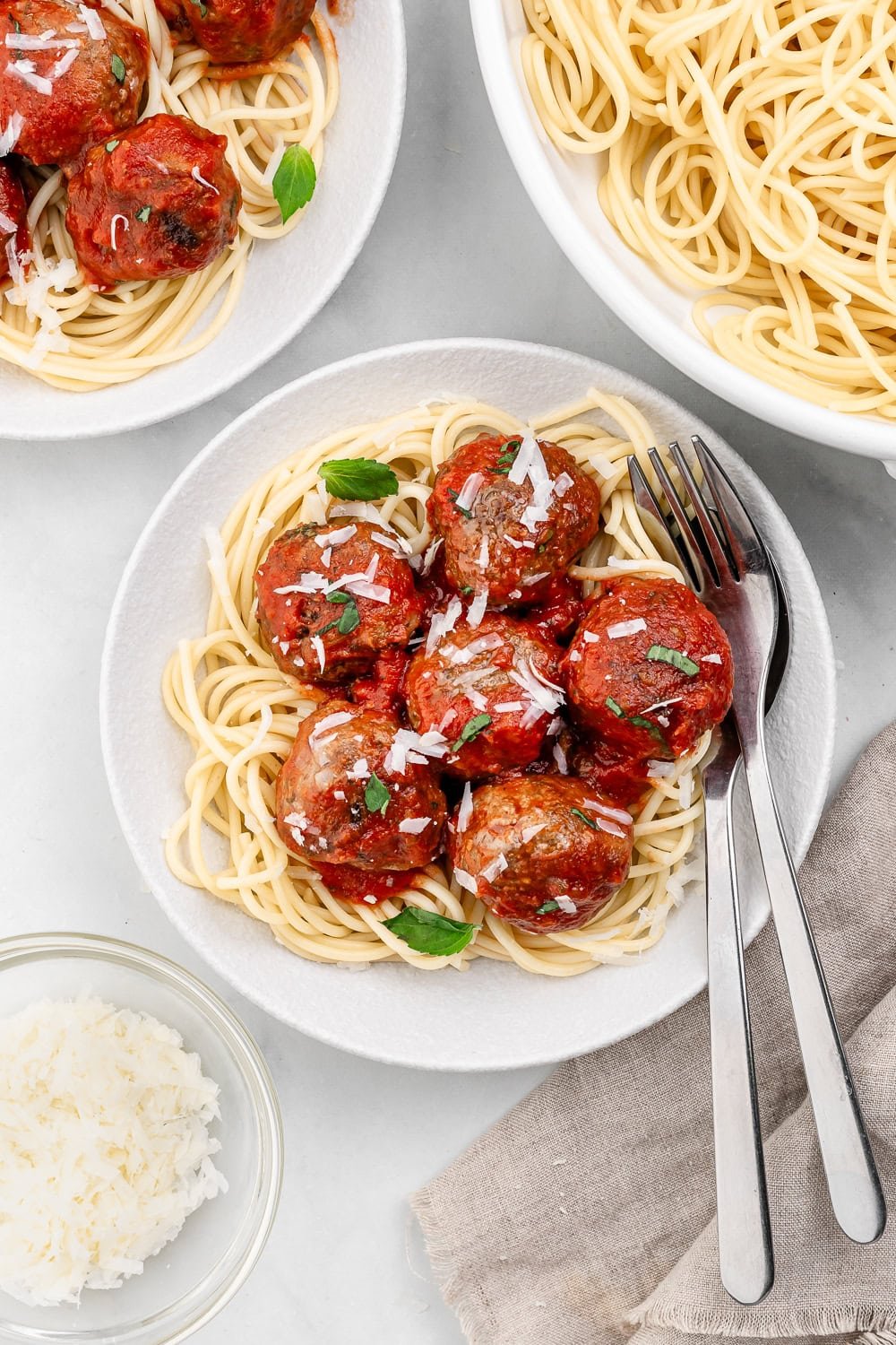 Finished bowl of meatballs over spaghetti with fork and spoon.