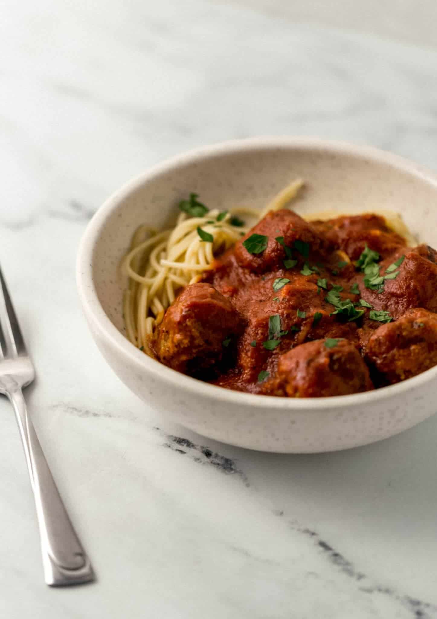 close up side view of spaghetti and meatballs in white bowl beside a fork 
