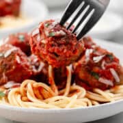Meatball on a fork held over a plate of spaghetti.