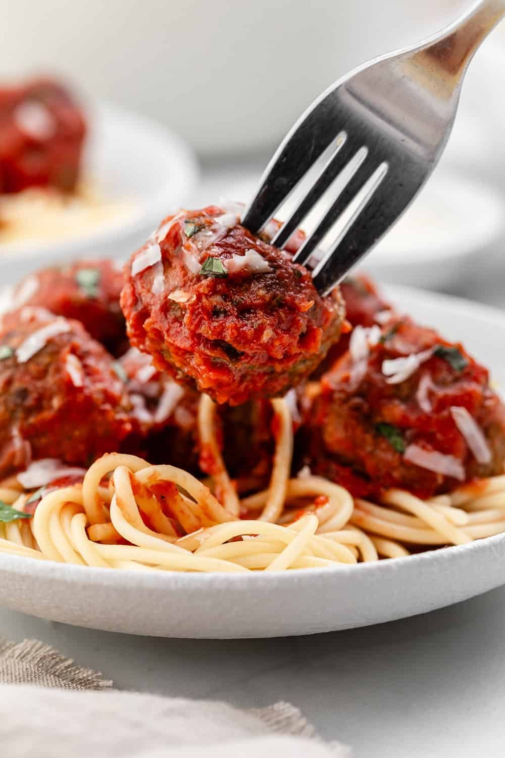 Close up view of fork with meatball on it over plate of pasta.