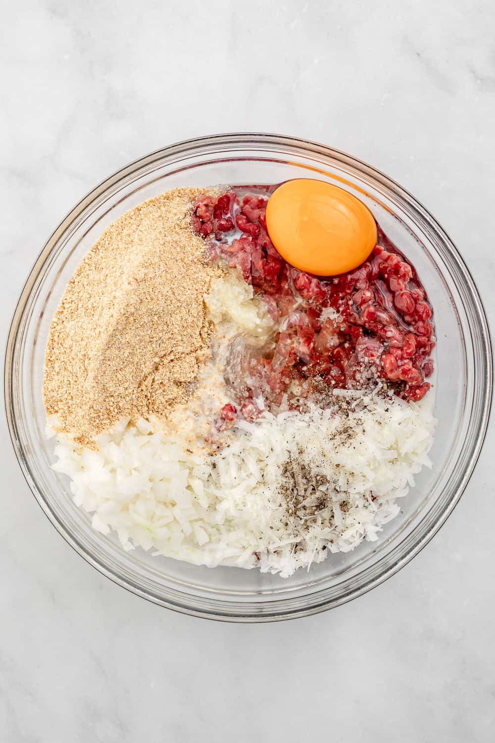 Ingredients to make meatballs added to glass mixing bowl.