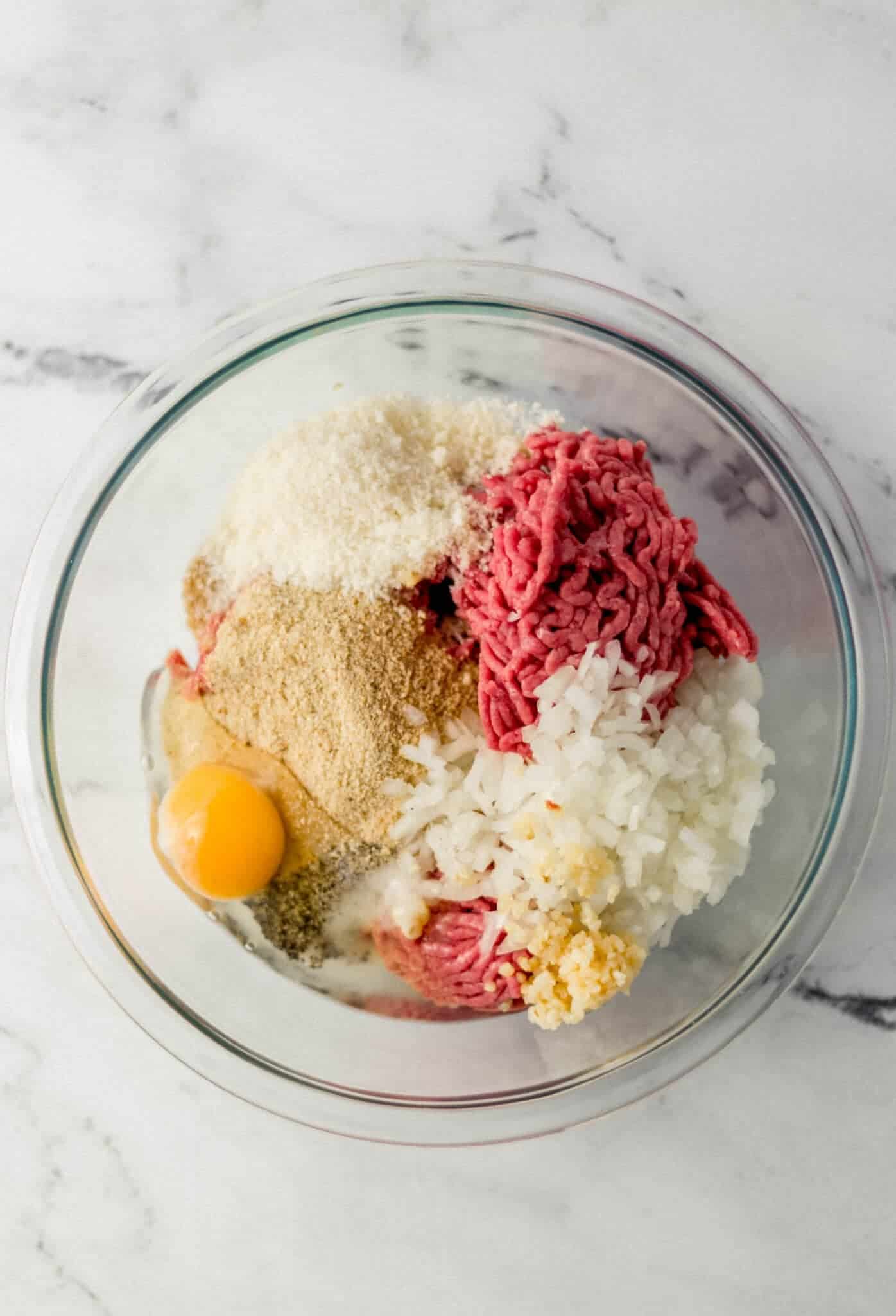 ingredients to make meatballs in glass mixing bowl 