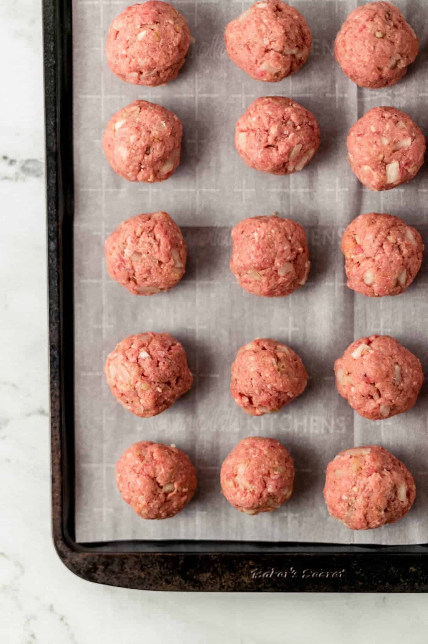 raw meatballs on parchment lined baking sheet
