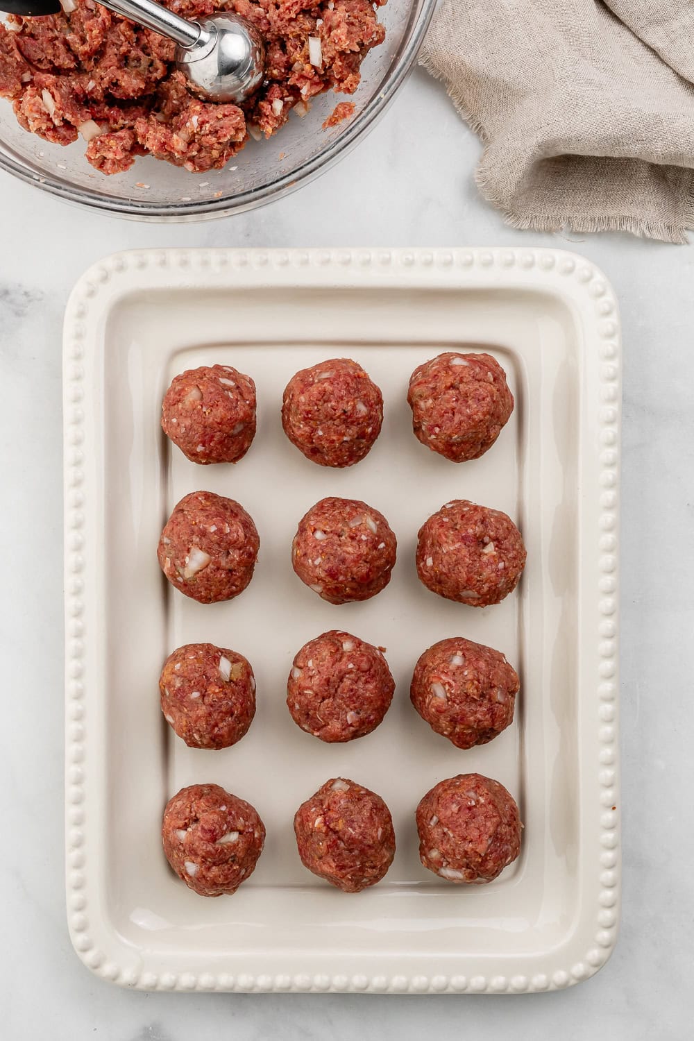 Meat mixture formed into meatballs on white platter.