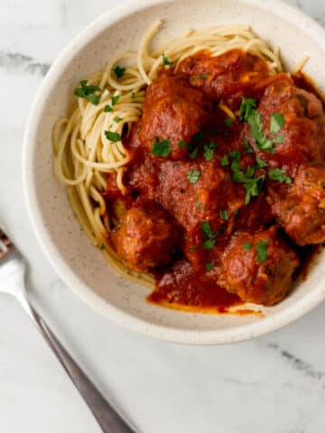 overhead view of spaghetti and meatballs in white bowl topped with parsley beside a fork