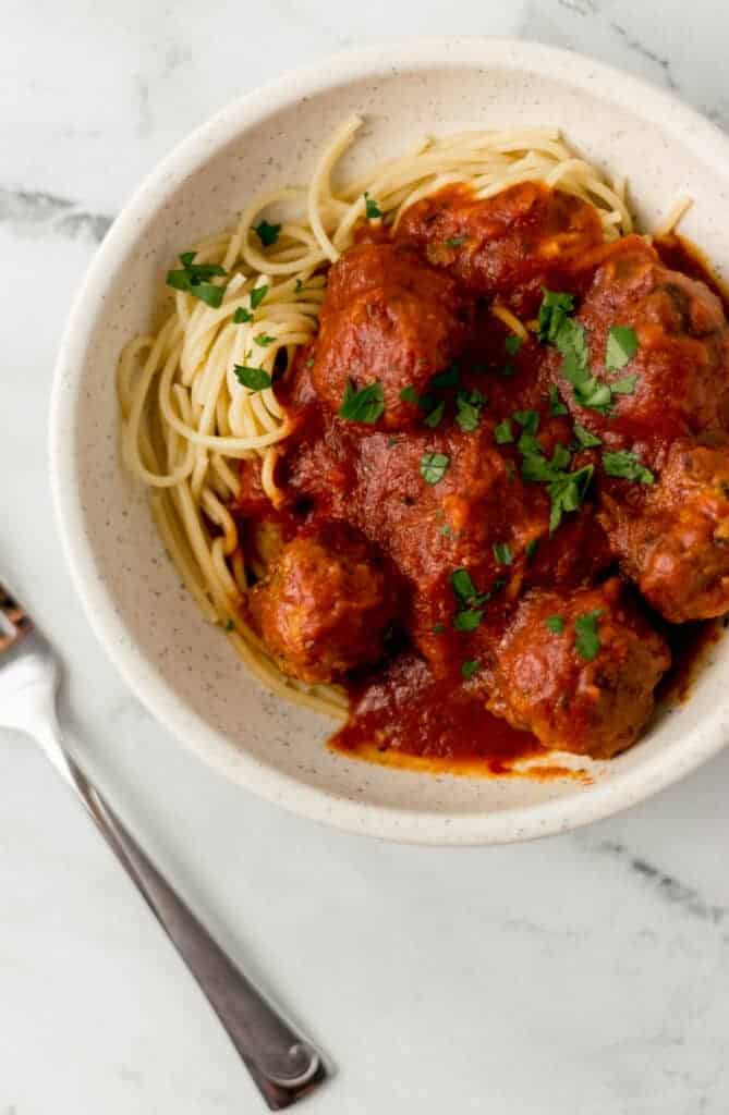 overhead view of spaghetti and meatballs in white bowl topped with parsley beside a fork