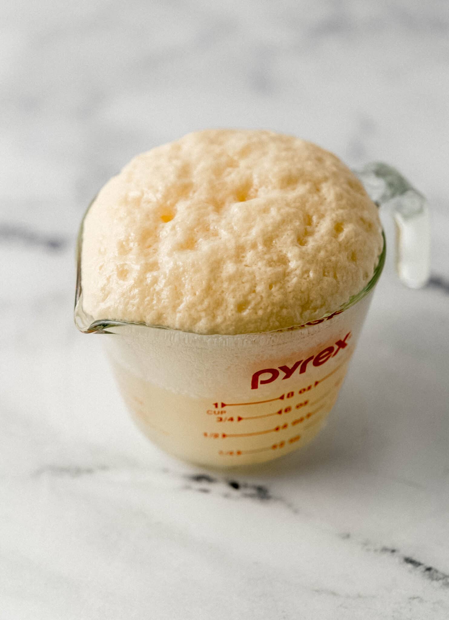 close up side view of proofed yeast mixture in glass measuring cup