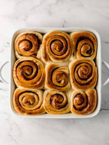 overhead view of finished vegan cinnamon rolls topped with glaze in white baking dish