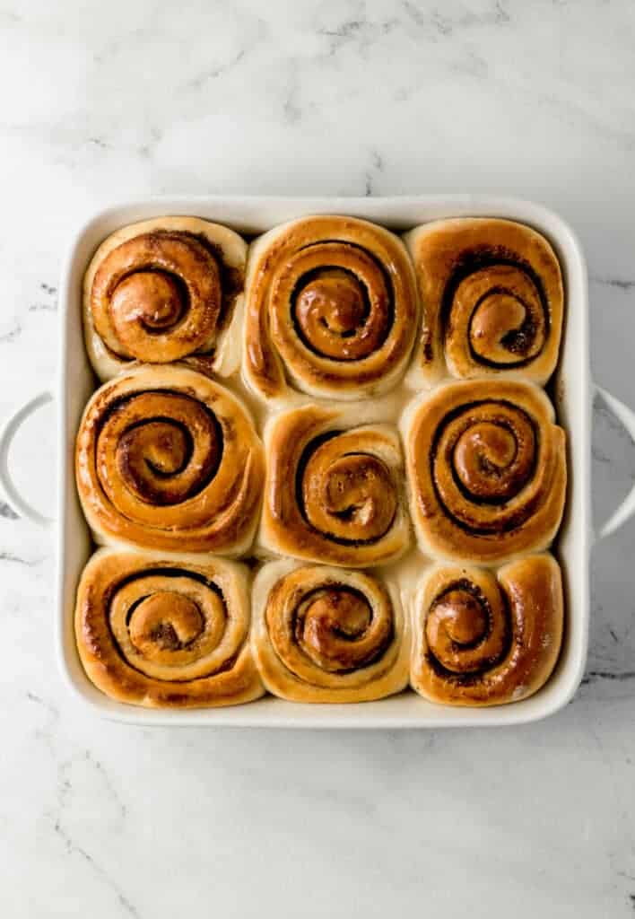 overhead view of finished vegan cinnamon rolls topped with glaze in white baking dish